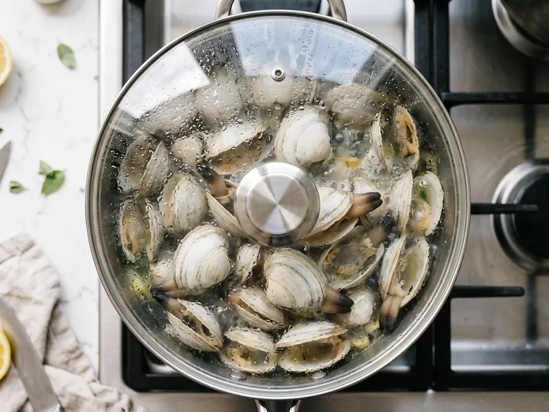 Myes entières dans un faitout couvert, la buée sur le couvercle de verre, les siphons sombres dépassant des coquilles